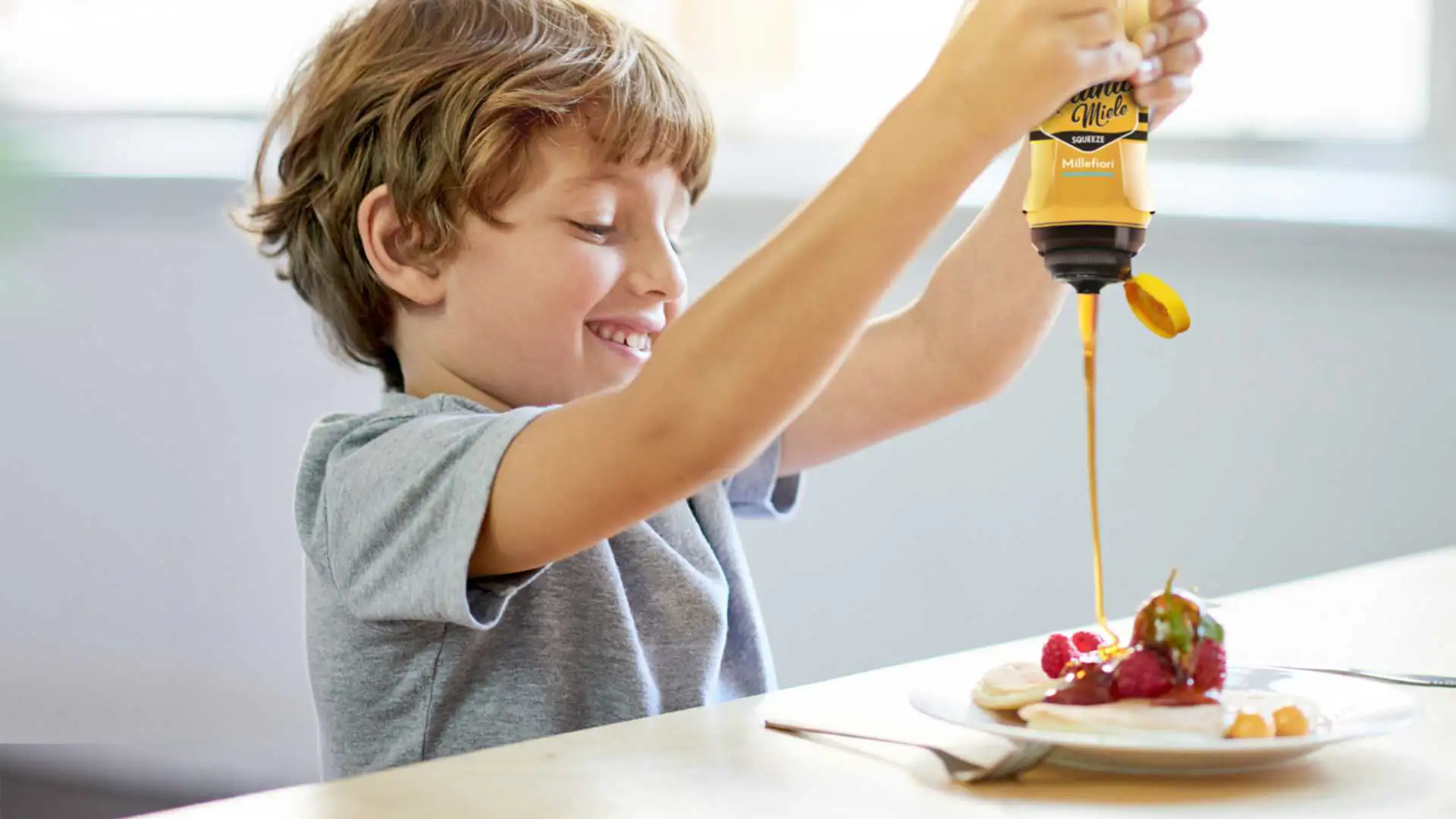 Bambino che versa miele Piana Miele in formato squeeze sui pancake, simbolo di consumo quotidiano pratico e piacevole del miele italiano di Apicoltura Piana SpA | DiBi Group